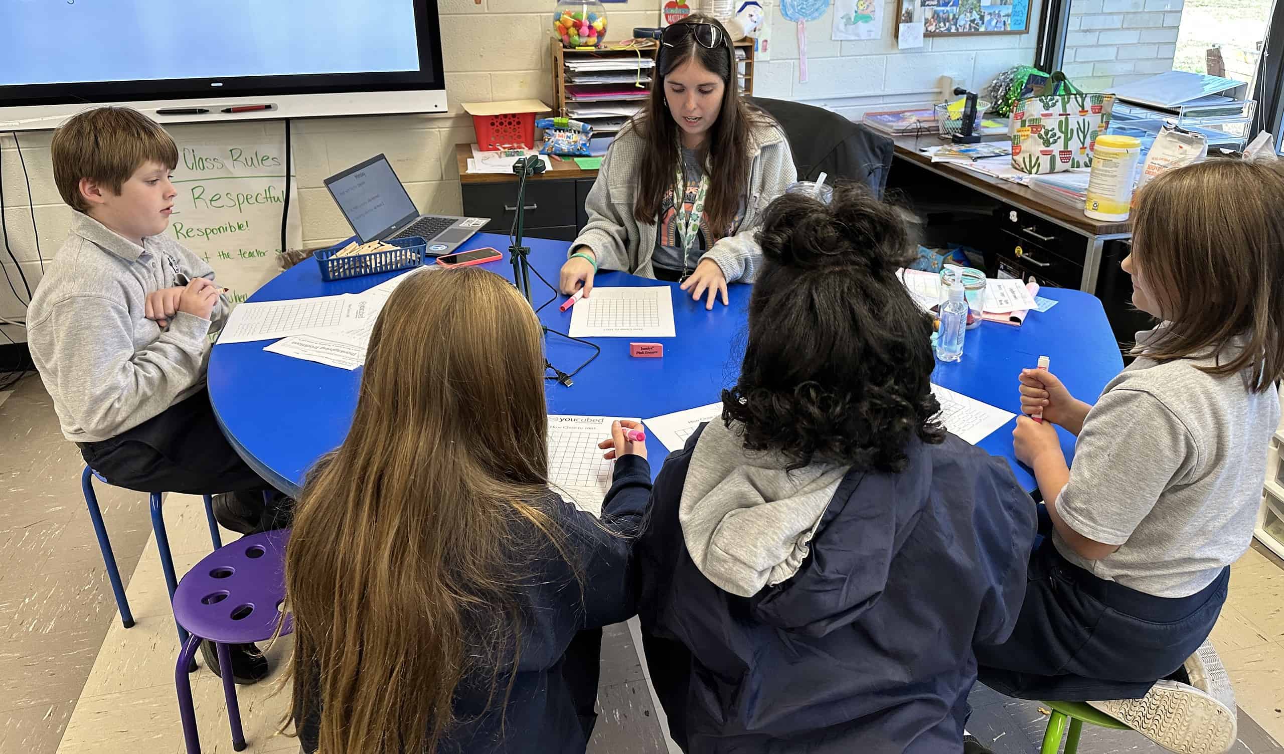 A third grade teacher working with a small group of four students at a semi-circle table