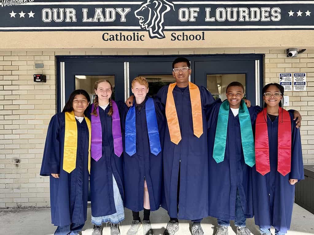 private middle school: six graduating 8th grade students in graduation gowns with stoles in their house colors (yellow, purple, blue, orange, green, and red)
