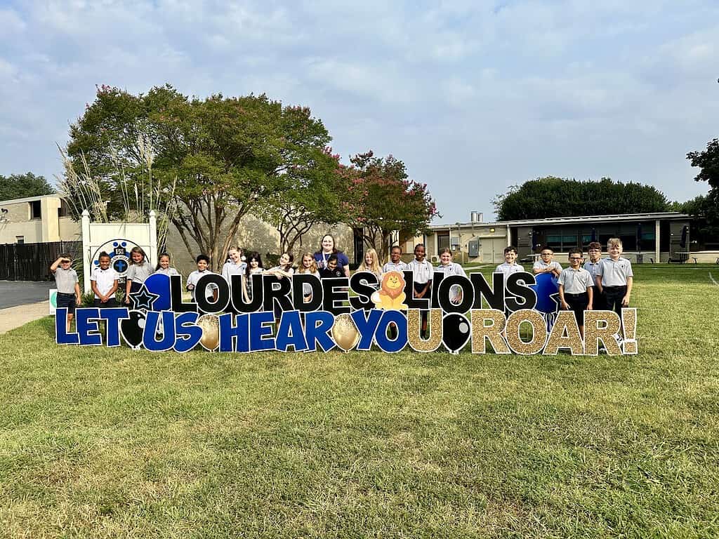 4th grade students behind a sign reading "Lourdes Lions, let us hear you roar!"